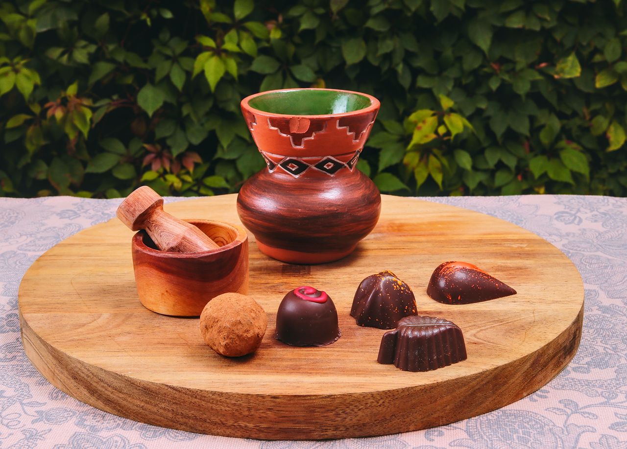 Services A selection of artisan chocolate pralines on a rustic wooden board with a decorative mortar and pestle.
